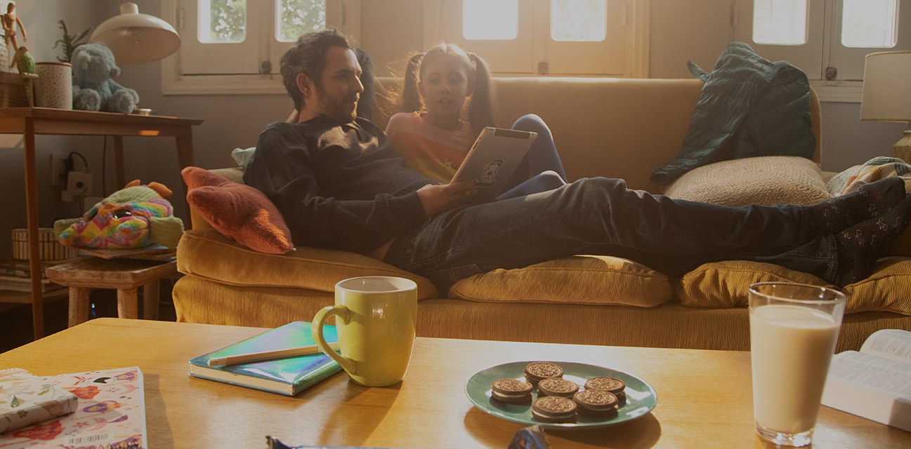 padre e hija disfrutando de una merienda con Oreo mientras leen un libro en el living.